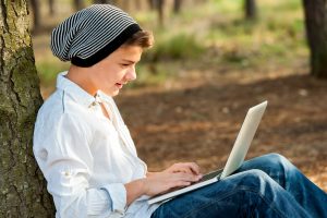 Portrait of teen boy chatting on laptop in park.