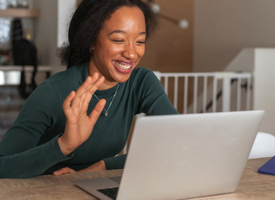girl smiling and waving to camera on laptop