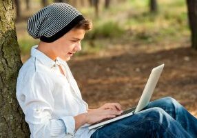 Portrait of teen boy chatting on laptop in park.